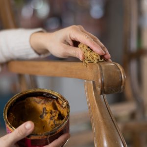 Close up of artisan hand applying light brown wax to old vintage chair in furniture workshop