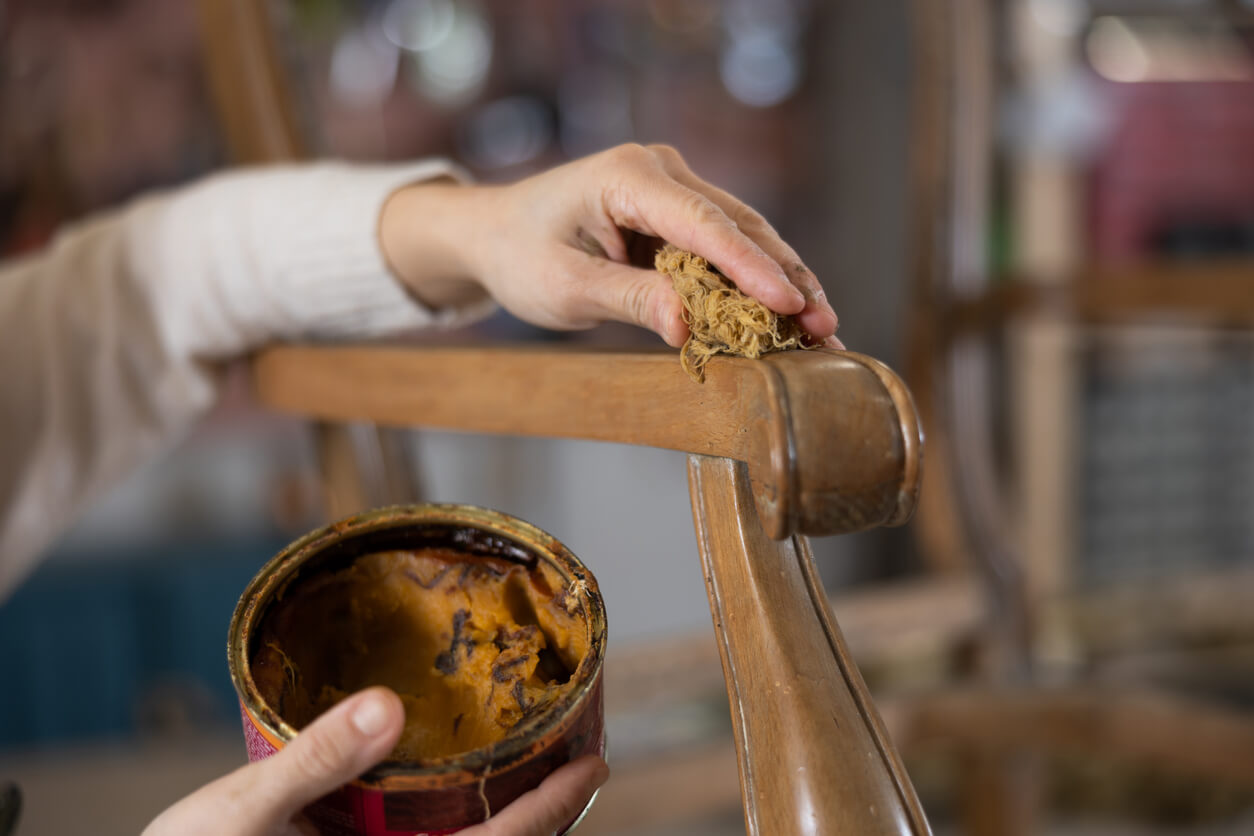 Close up of artisan hand applying wax to old vintage chair in furniture workshop Close up of artisan hand applying light brown wax to old vintage chair in furniture workshop
